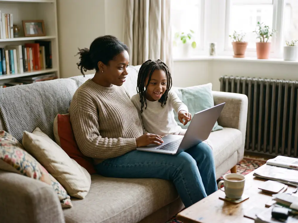 A mum and her daughter on the sofa looking at a laptop, the daughter pointing at the screen